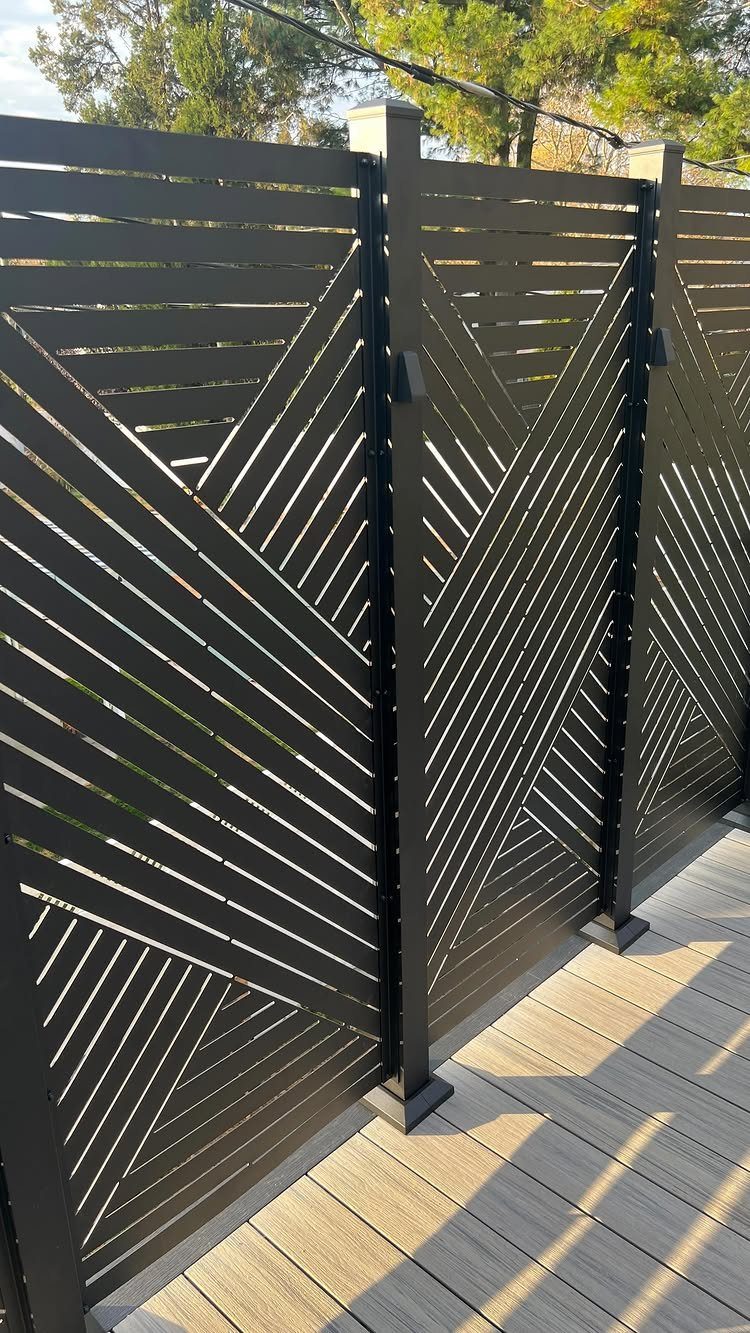 Black geometric slatted privacy screens installed on a light wood outdoor deck.