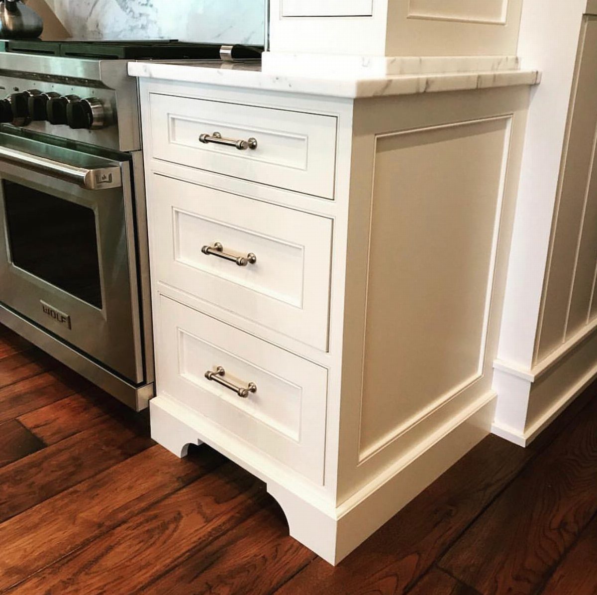 White kitchen cabinets with silver handles, marble countertops, and decorative molding on the side panel.