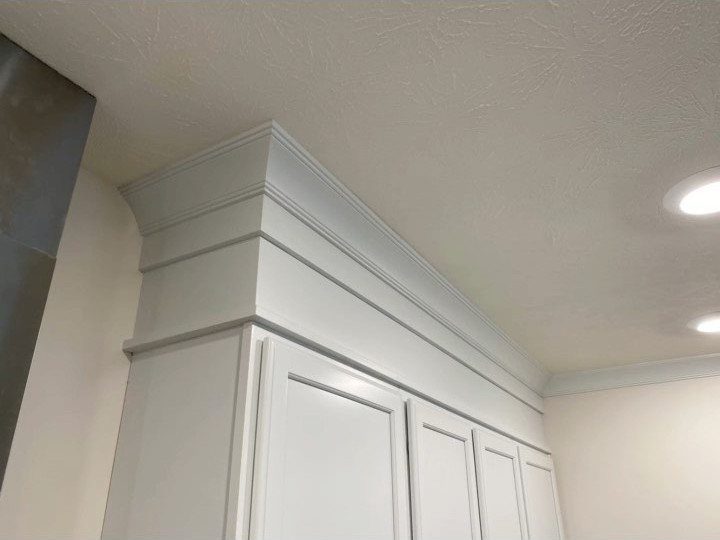 White kitchen cabinets with decorative tiered crown molding installed at the ceiling line.