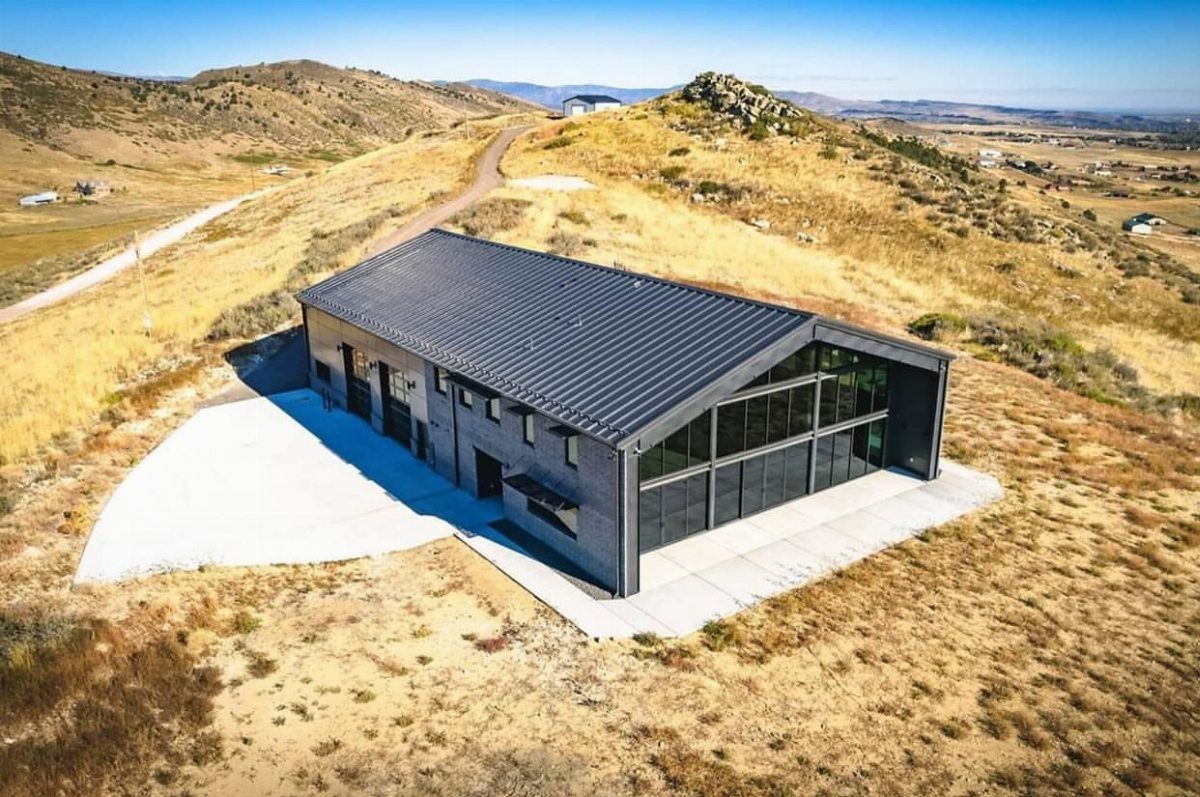 Black metal barndominium with large glass windows sitting on a dry grassy hill.