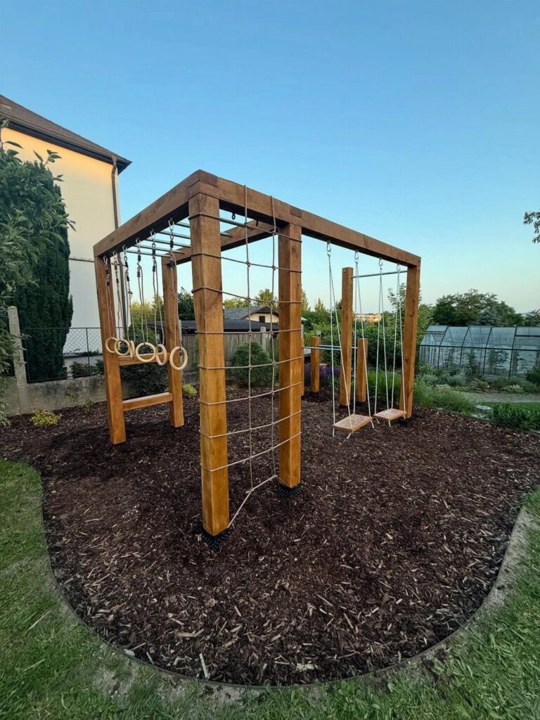 Wooden backyard playset with swings and climbing rings on dark mulch.