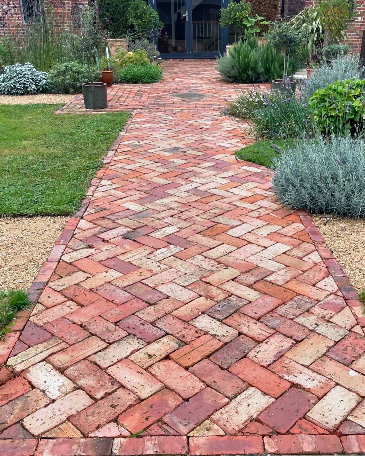 A multi-colored brick pathway laid in a herringbone pattern through a green garden.