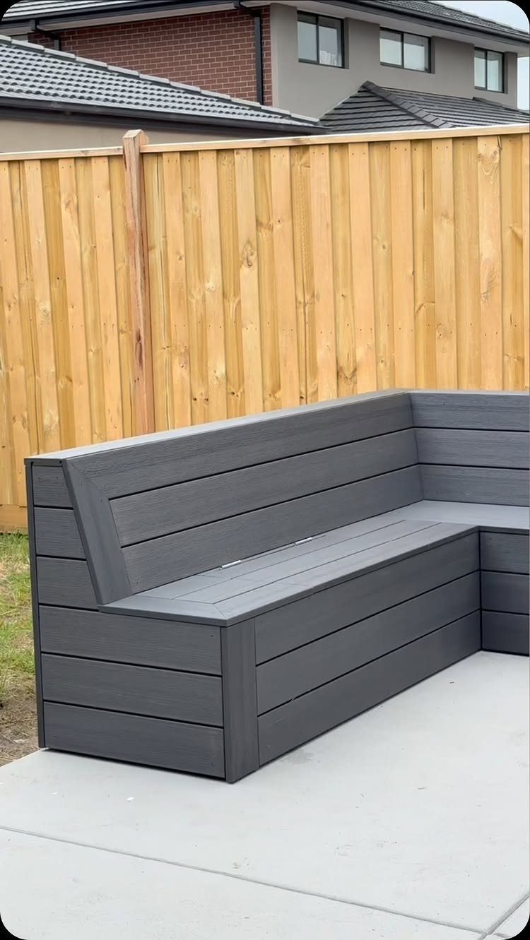 A dark grey L-shaped wooden built-in bench on a concrete patio.