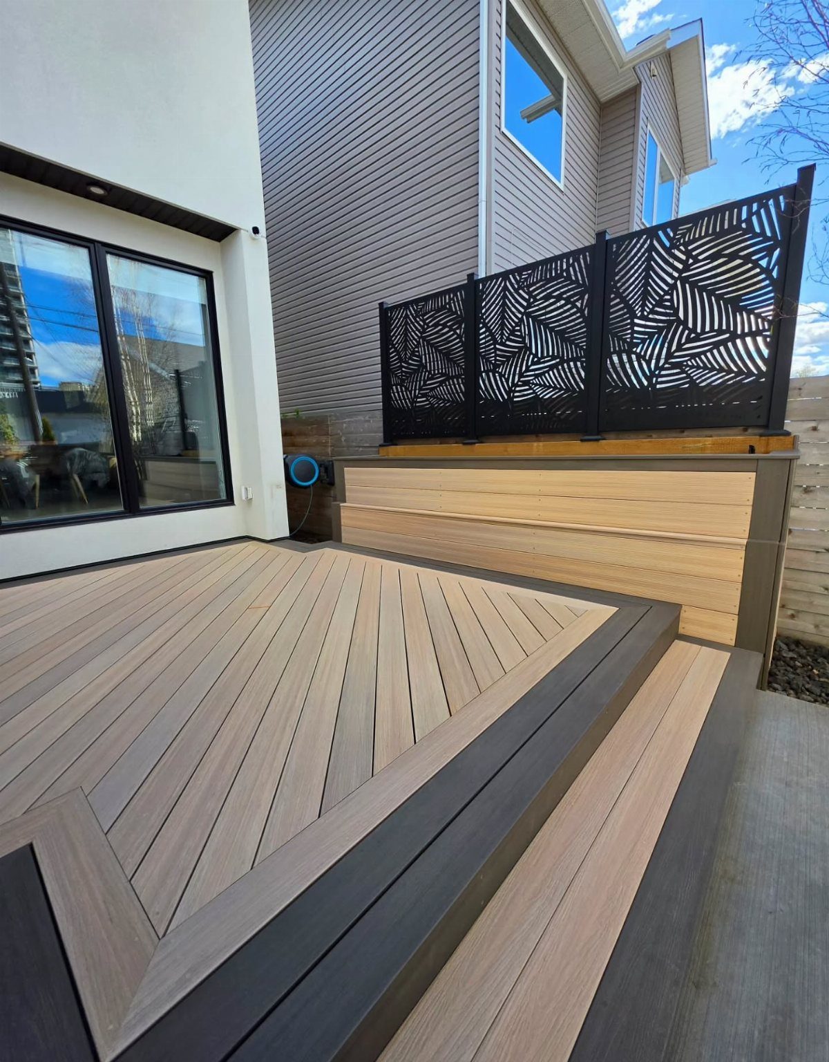 Modern outdoor wooden deck featuring a geometric chevron plank pattern with dark grey borders and steps.