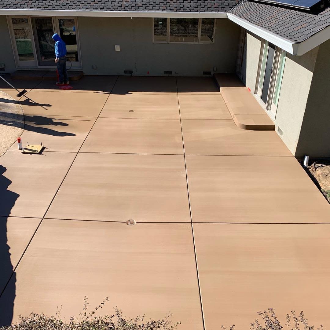 12 Concrete Patio Ideas for Stamped, Colored and Geometric Designs 2 A wide expanse of smooth, tan colored concrete patio next to a residential house.
