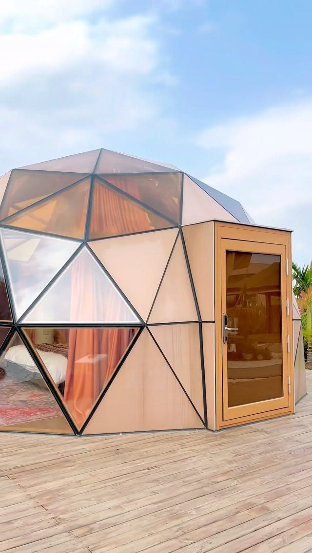 Glass Dome Garden Design: 10 Ideas for Every Outdoor Space 10 A copper-toned geodesic dome structure with glass panels standing on a wooden deck under a blue sky.