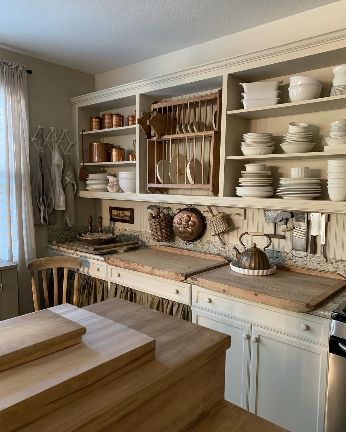 Open kitchen shelves displaying white ceramic dishes and copper pots above a wooden countertop.
