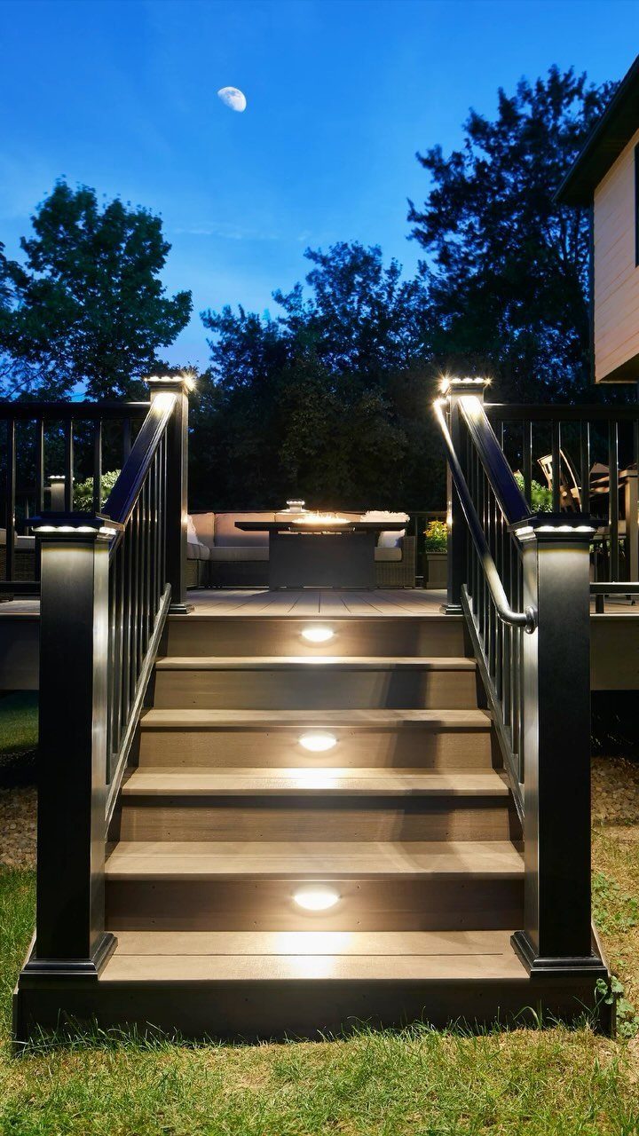 Wooden deck stairs featuring integrated circular LED lights on each step under a twilight sky.