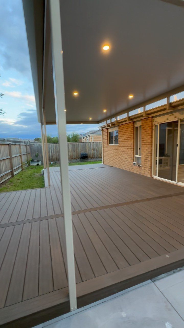 A wide wooden outdoor deck with dark border accents under a covered patio roof.