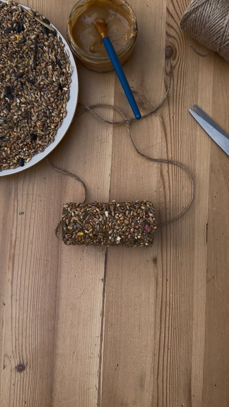 A handmade bird seed feeder on a wooden table with birdseed and crafting supplies.