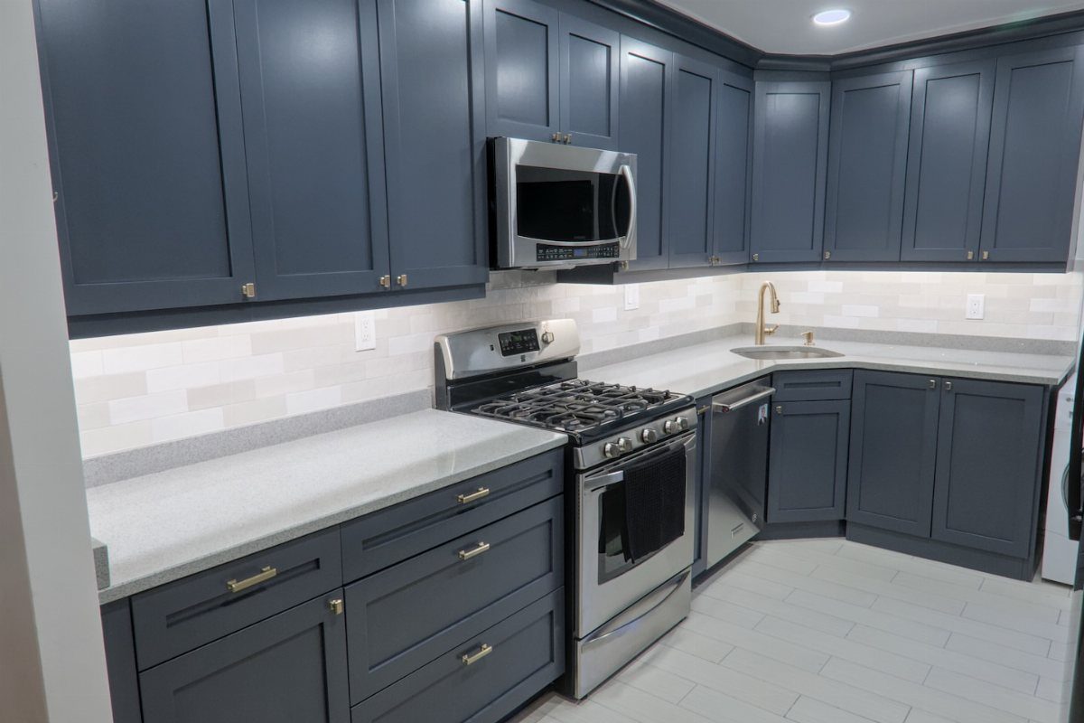 Dark grey painted kitchen cabinets with light grey countertops and stainless steel appliances.