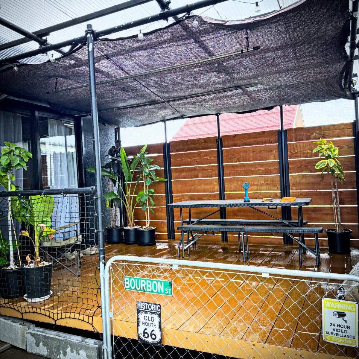 Black mesh netting stretched over a wooden deck area with a picnic table and potted plants.