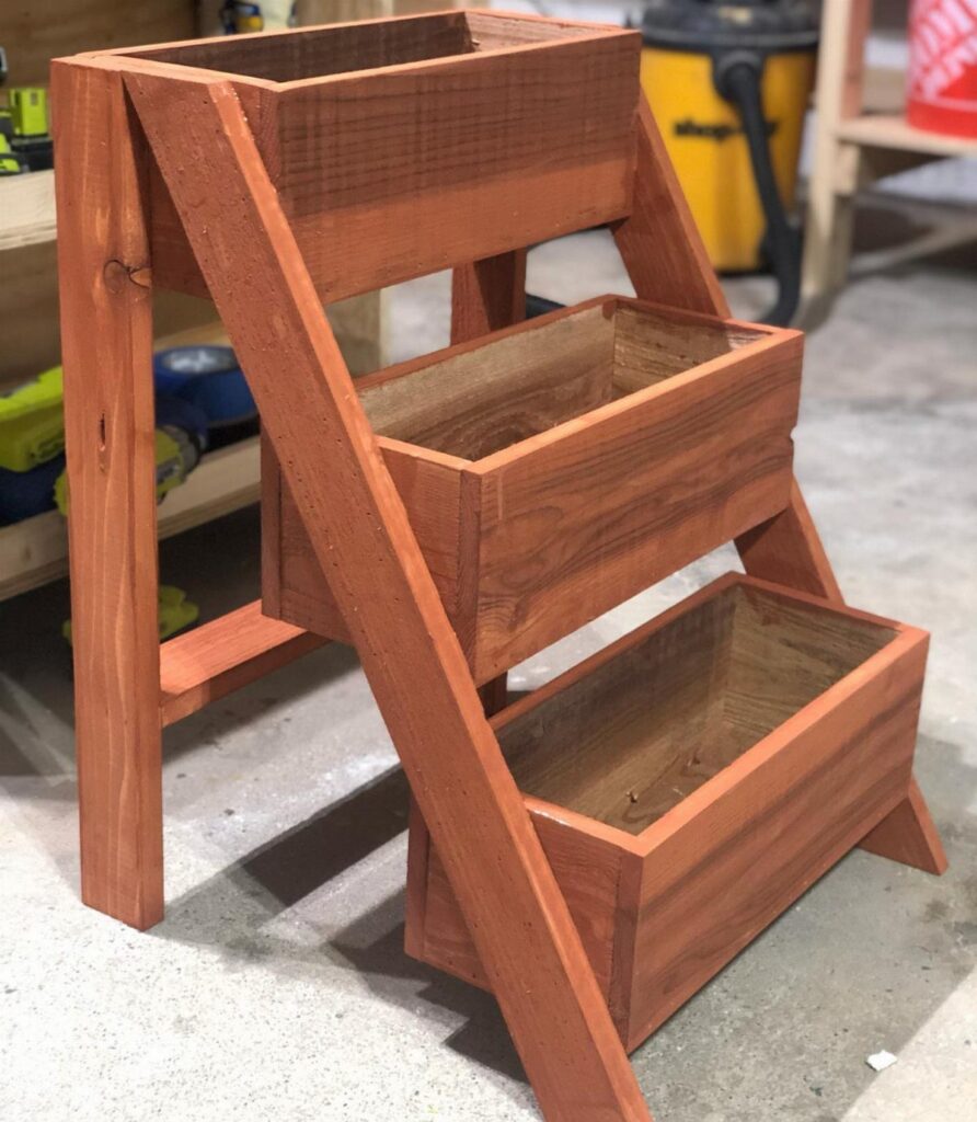 A three-tiered reddish-brown cedar wood planter stand standing in a workshop.
