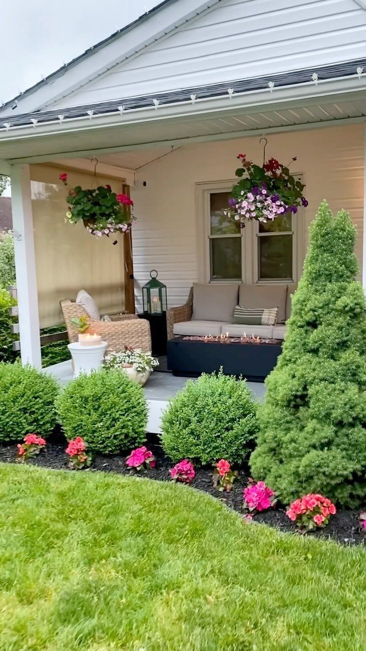13 Cottage Garden Front Yard Ideas for Curved Paths to Climbing Roses 11 Green shrubs and pink flowers line a white porch with outdoor seating and hanging baskets.