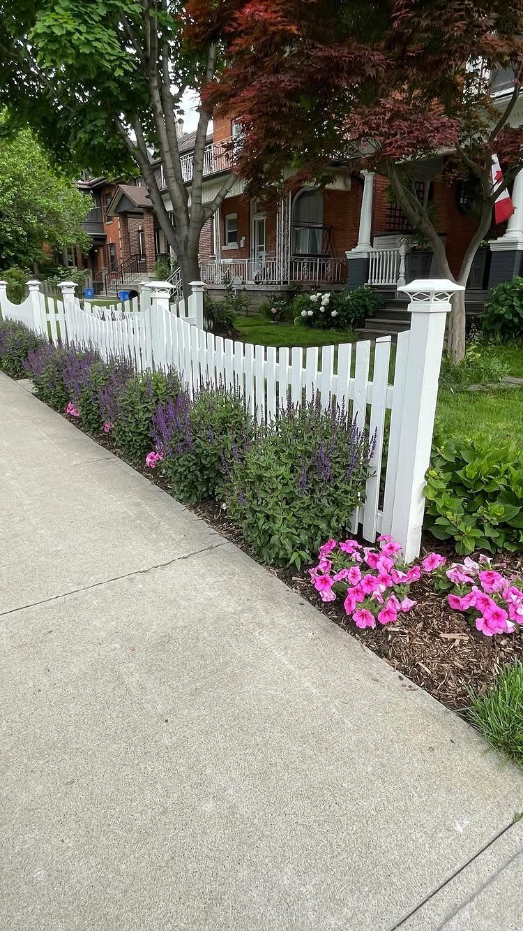13 Cottage Garden Front Yard Ideas for Curved Paths to Climbing Roses 6 Purple lavender and pink flowers planted along a white picket fence next to a sidewalk.