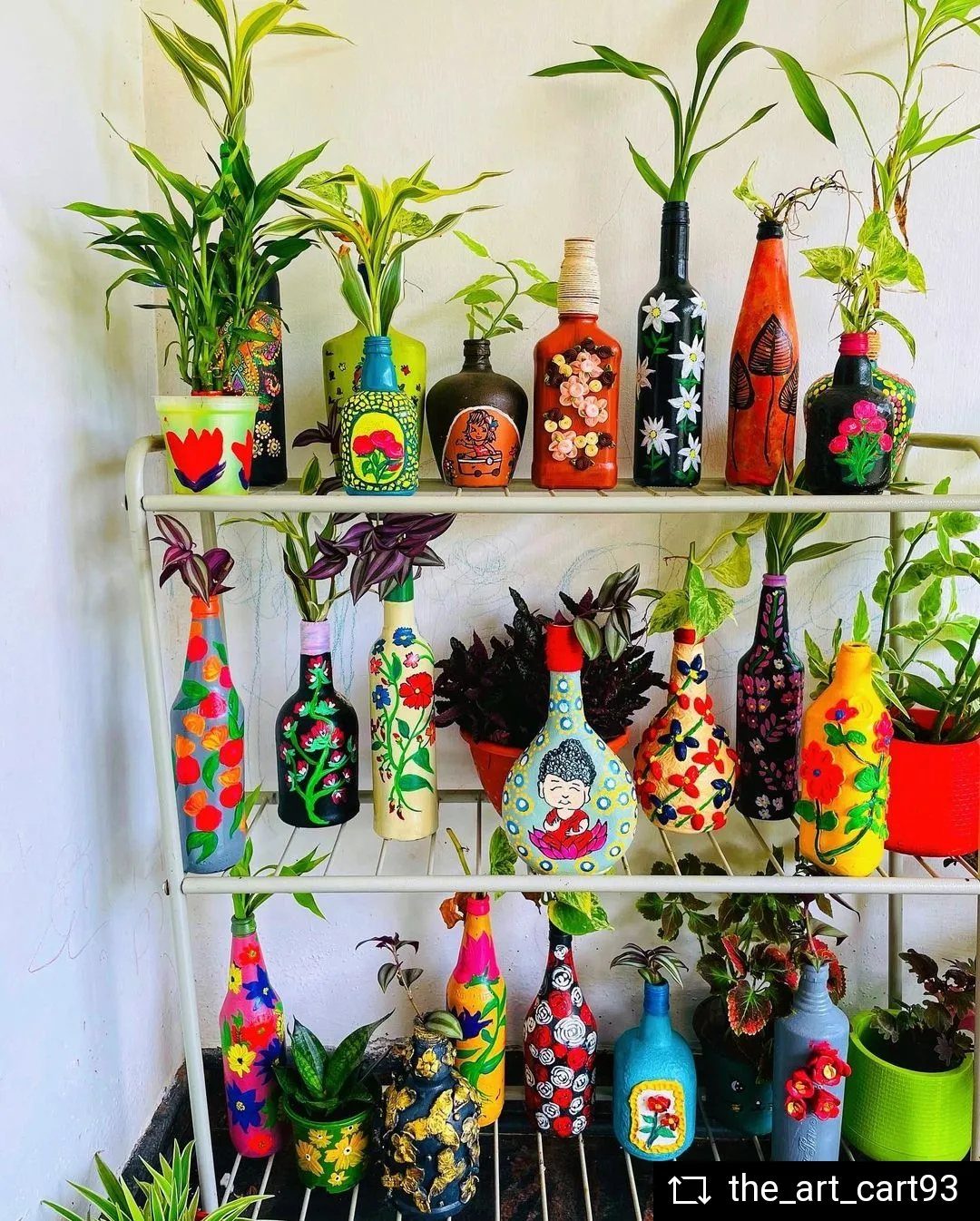 Hand-painted colorful glass bottles used as plant vases arranged on a white metal shelf.