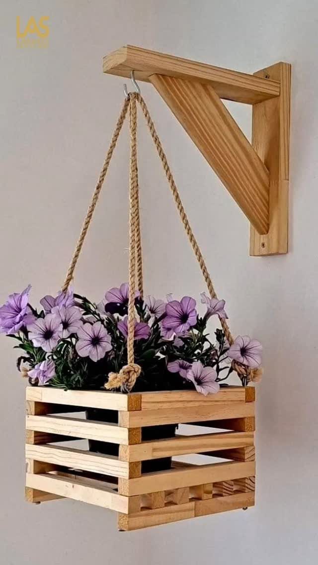 A wooden hanging planter box filled with purple petunias suspended by ropes from a wall bracket.