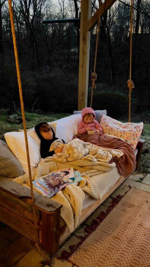 16 DIY Backyard Kids Ideas for Outdoor Summer Fun 16 Two children wrapped in blankets relaxing on a large wooden outdoor swing bed.