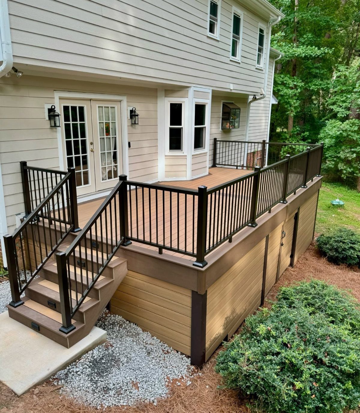 A large wooden deck with black railings and tan horizontal composite skirting panels attached to a house.