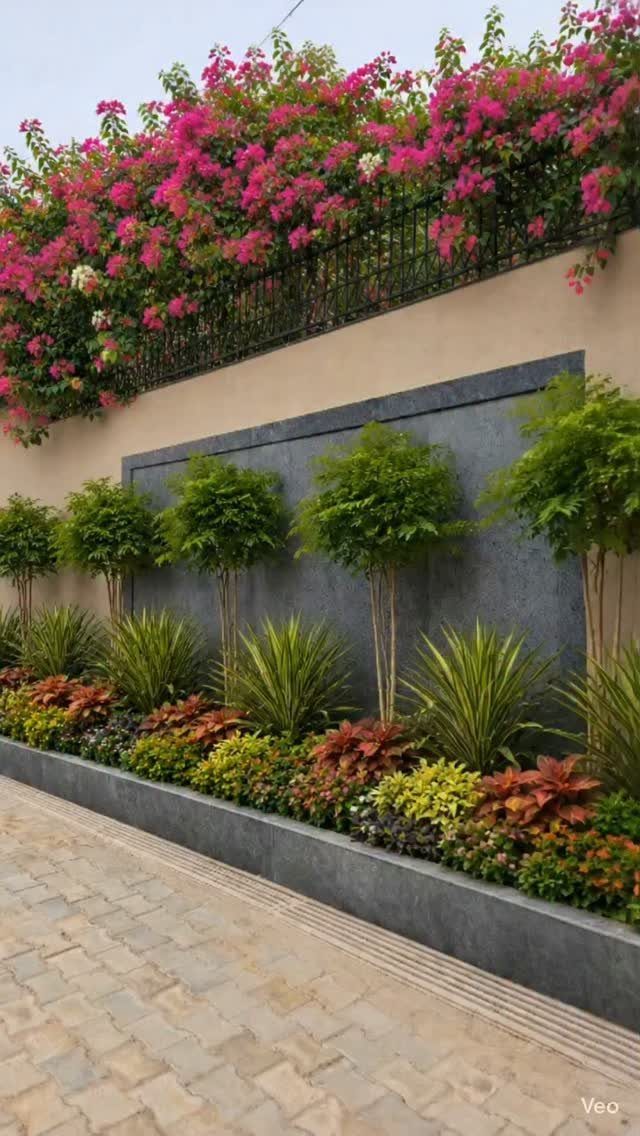 A long raised garden bed with ornamental grasses and colorful foliage along a stone walkway.