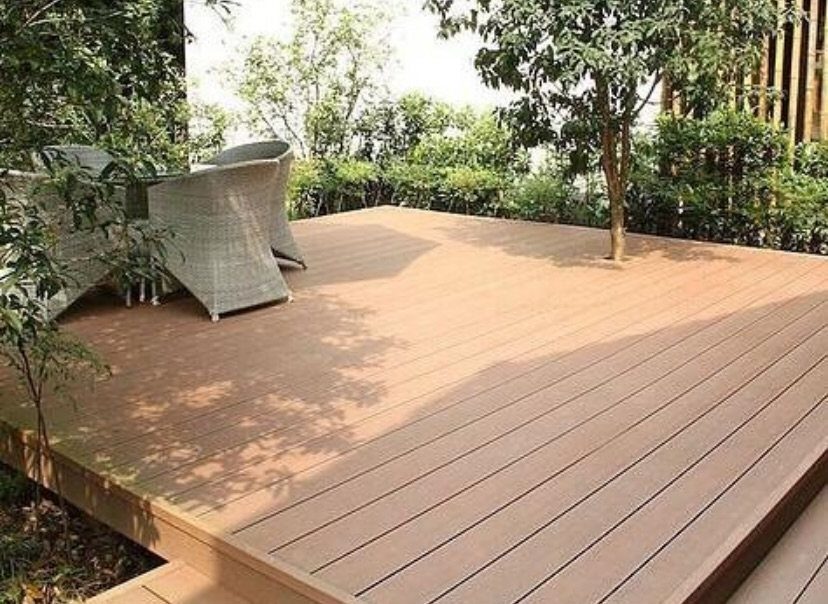 Light brown wooden deck planks surrounded by green trees and two wicker chairs.