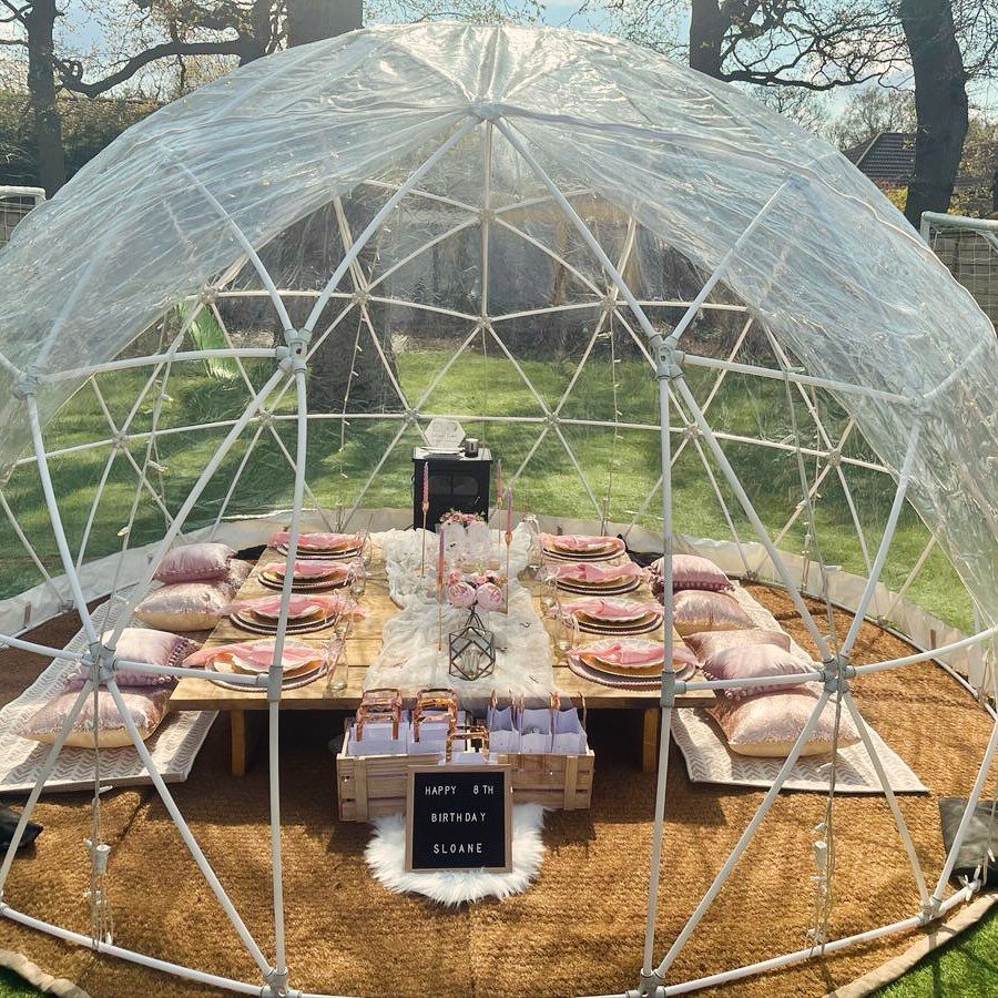 Glass Dome Garden Design: 10 Ideas for Every Outdoor Space 3 A clear geodesic dome containing a low wooden dining table set with plates and cushions on a lawn.