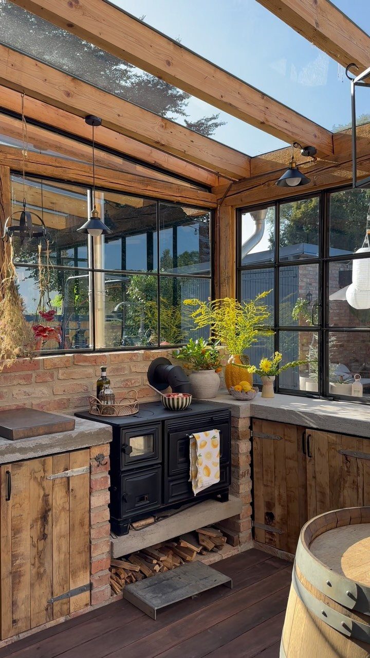 A rustic greenhouse kitchen with a black wood-burning stove and wooden cabinetry.