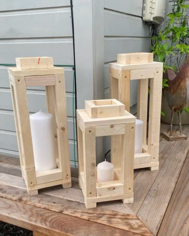 Three handmade wooden lanterns with white pillar candles sitting on a wooden deck outdoors.