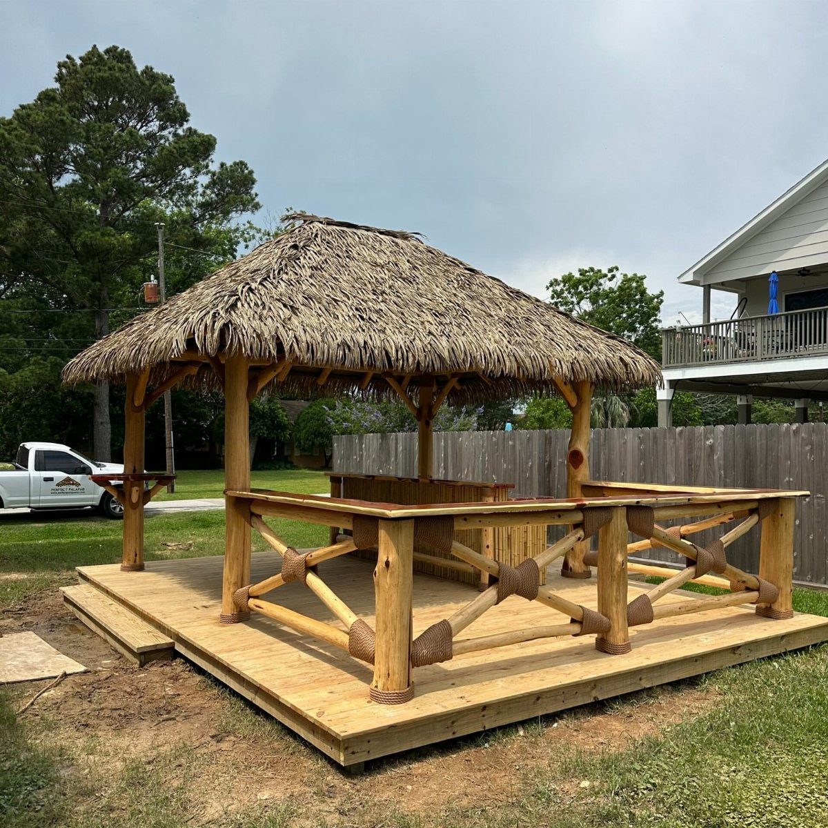 A wooden palapa with a thatched roof and built-in bar on a deck.