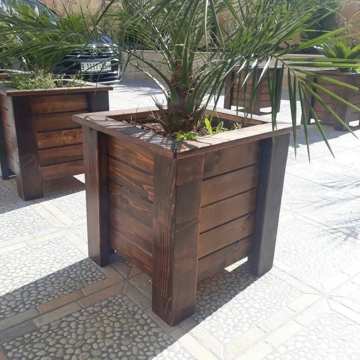 Large dark stained wooden planter boxes containing green palm plants on a stone patio.