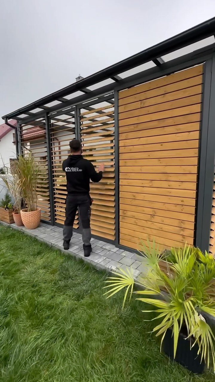 A man installing wooden slats into a black metal frame structure next to a green lawn.