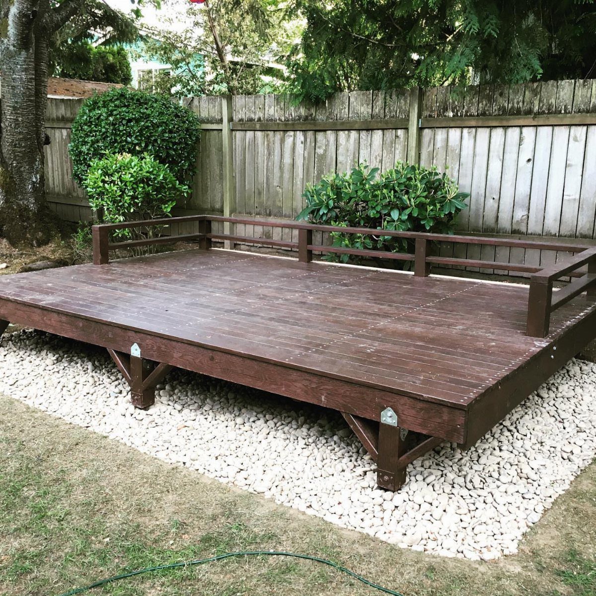 A dark brown wooden deck platform with a low railing sits on white gravel.