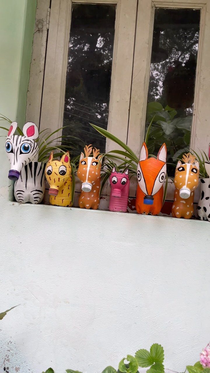 Six colorful animal-shaped planters with green plants sitting on a white windowsill.