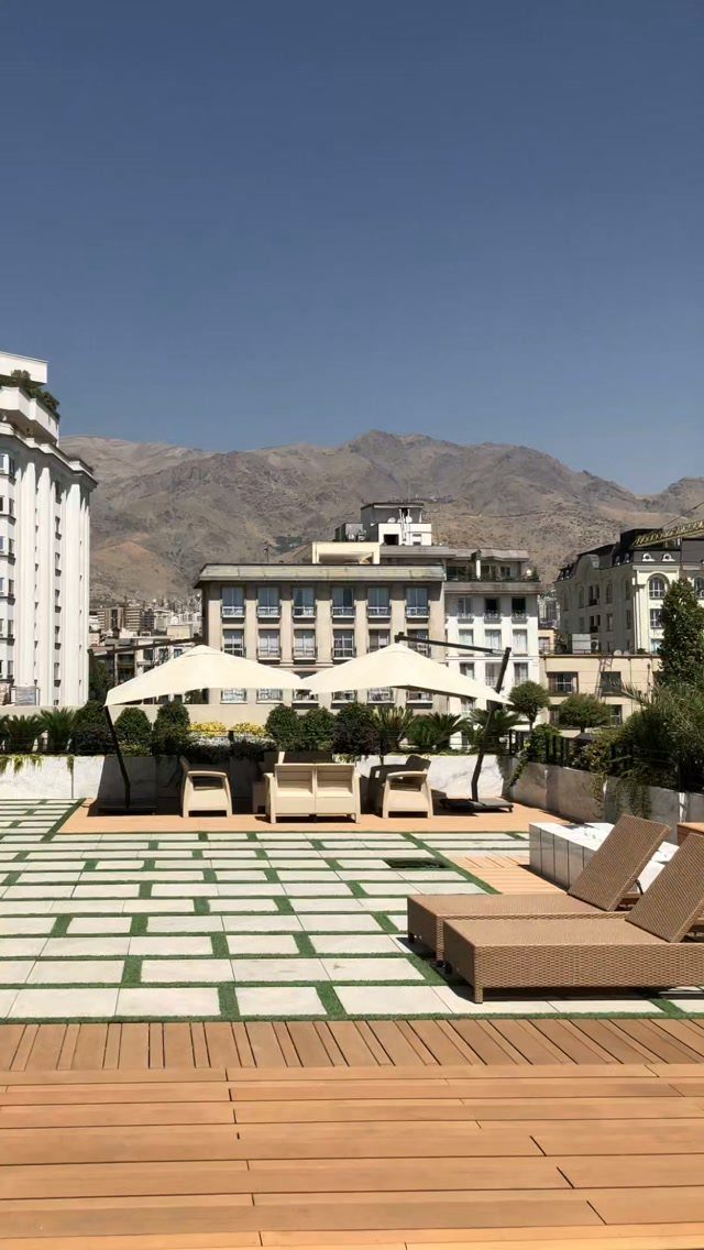 Rooftop terrace with wooden decking, lounge furniture, and mountains in the background.