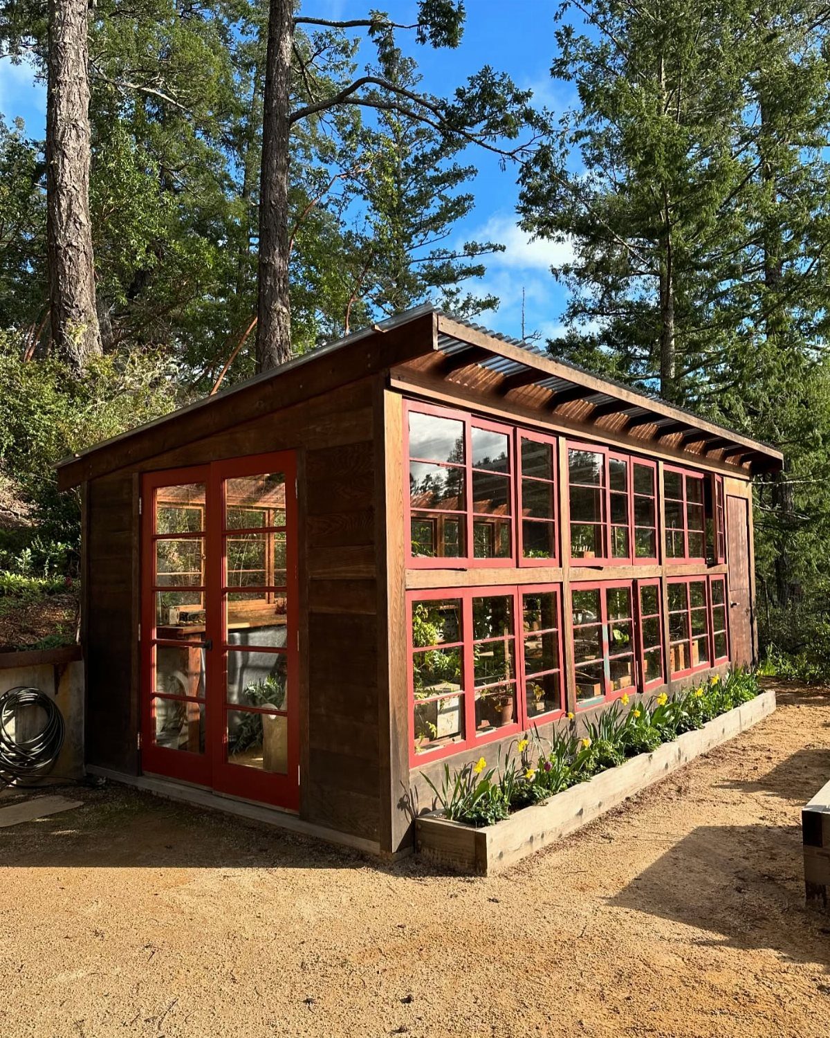 A wooden garden building featuring numerous red-framed glass windows and a matching glass door.