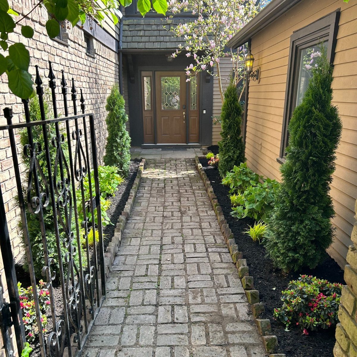 Stone paver walkway lined with green shrubs and colorful flowers leading to a house entrance.
