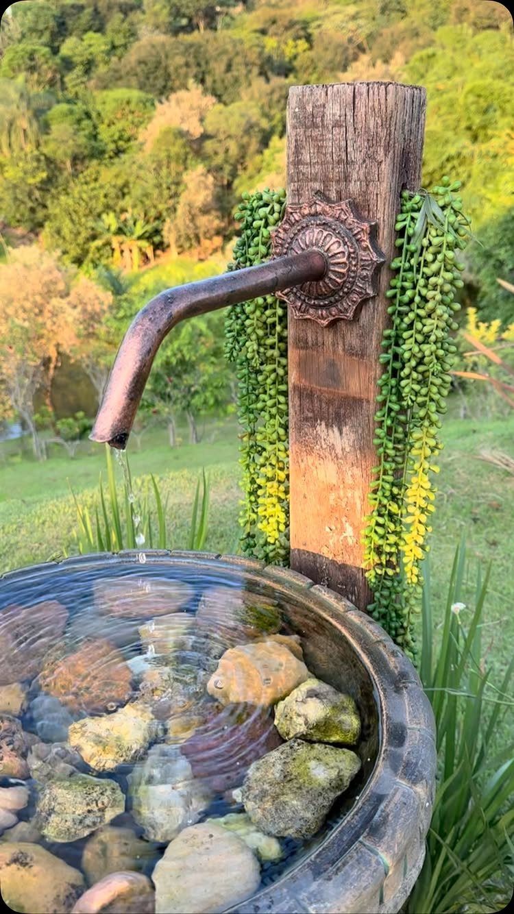 A rustic bird bath with a metal spout dripping water into a stone basin with rocks.